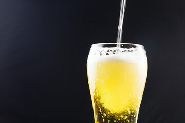 pouring beer into a takan on a dark background. beer foam flows down the walls of the glass