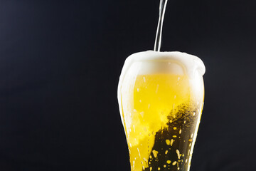 pouring beer into a takan on a dark background. beer foam flows down the walls of the glass