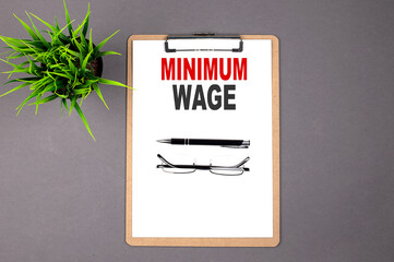 MINIMUM WAGE on the brown clipboard on the grey background. Business concept