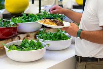 A man chooses a salad from the fresh herb salad bar at the hotel's buffet. healthy food concept