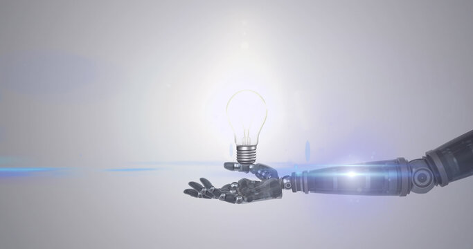 Image of illuminated light bulb over hand of robot arm, with moving light on grey background
