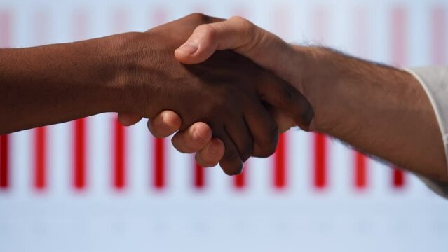 Handshake: two businessmen shaking hands on the background of business statistics