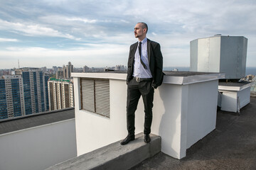 a man in a black suit with a tie stands on the roof and looks ahead