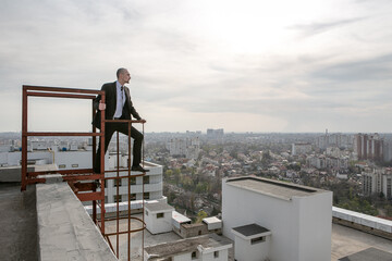 a man in a black suit with a tie stands on the edge of the fire escape and looks at the panorama of the city
