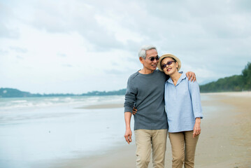 Asian Senior couple  walking on the beach enjoy life  at sunrise