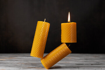 Three yellow beeswax balancing candles are on the table. Eco product on a dark background