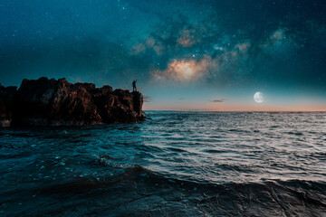 silhouette of a person on the rocks over the ocean at night with the milky way in the background
