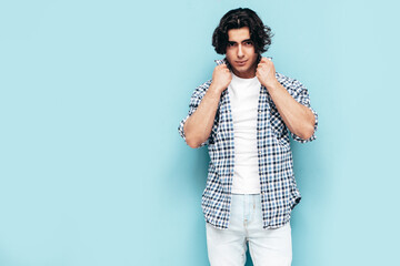 Portrait of handsome confident model. Sexy stylish man dressed in checkered shirt and jeans. Fashion hipster male posing near blue wall in studio. Isolated