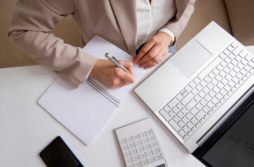 businesswoman counts the budget and makes notes in a notebook on the desktop with a calculator and a laptop.