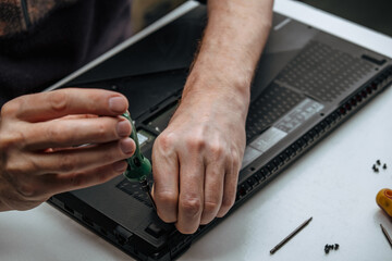 close-up of the repairman's hands unscrewing the screws from the laptop case with a screwdriver for...