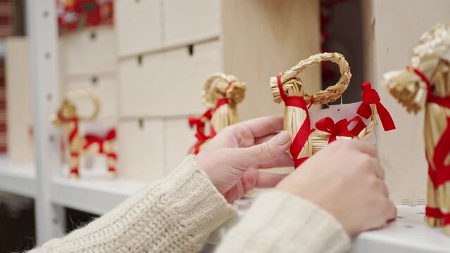 a woman's hand takes from a shelf a Christmas goat made of straw, decorated with a red ribbon