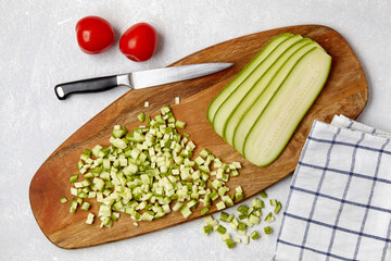 Courgette zucchini diced sliced and red tomatoes on a wooden cutting board on a white concrete table