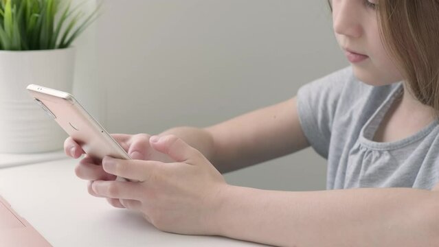 Kid girl using texting mobile phone or chat in home in the morning and sunlight, side view. Close up of child hands with cellphone. Wireless technologies, communication in social networks