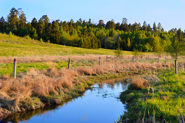 a rural landscape with a stream in which the blue sky is reflected