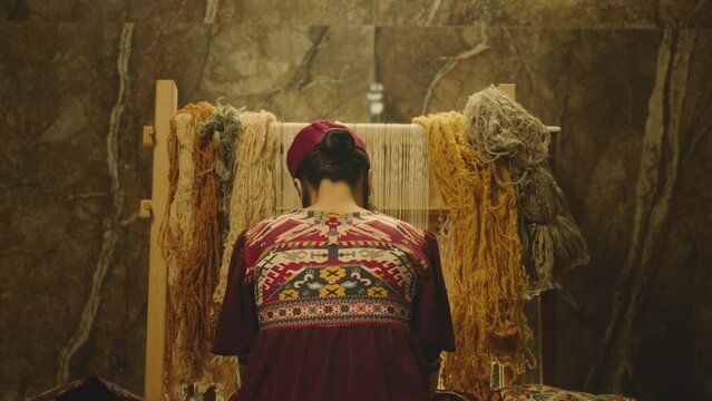 A Woman weaving traditional Asian carpet . Handmade carpet embroidery . Back view of Woman create a pattern using multi-colored threads . Rear view . Weaving machine . Needlework . Carpet-makers 