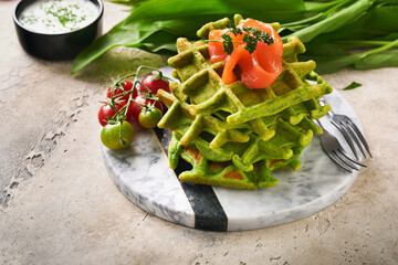 Green Belgian waffles. Spinach or wild garlic or pesto waffles with red salmon and cream sauce on grey concrete table background. Delicious breakfast, snack, brunch. Mock up. Selective focus.