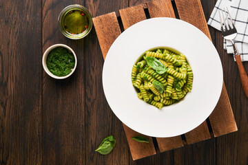 Italian Fusilli Pasta with Pesto. Fusilli pasta with basil pesto and herbs, parmesan cheese, basil and garlic on white plate on old wooden table background. Top view. Copy space. Mock up.