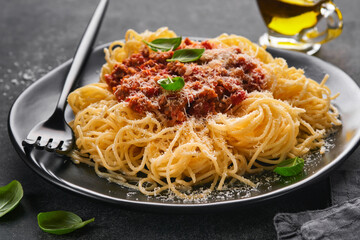 Classic spaghetti pasta Bolognese. Tasty appetizing italian spaghetti with bolognese sauce, tomato sauce, cheese parmesan and basil on black plate on dark slate, stone or concrete table background.