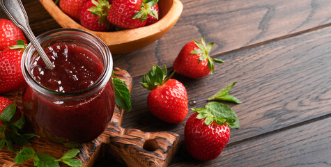 Strawberry jam. Strawberry jam in glass jar with fresh berries plate on an old wooden dark table background, closeup. Homemade strawberry fruity jam. Top view with copy space.