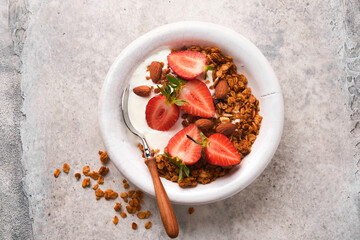 Granola. Bowl of homemade granola with yogurt and fresh berries strawberry for breakfast in a white bowl on old gray concrete background table background. Top view flat lay background.