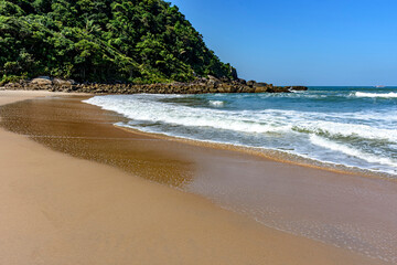 Paradisiacal rocky beach with clean and calm waters surrounded by forest and hills in Bertioga coast of Sao Paulo state, Brazil