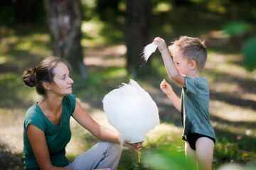 Obraz premium Cute european boy son and mom eating cotton candy in the park together, lifestyle