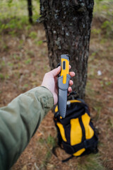 A bushcraft knife lies in a man's hand, a tactical knife with a plastic handle in the sheath, a yellow handle.