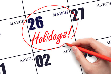 Hand drawing a red circle and writing the text Holidays on the calendar date 26 March. Important date.