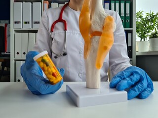 Doctor holds pills and model of the knee joint for bone treatment