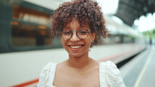 close-up portrait of a young woman in glasses stands on the platform next to the train and smiles
