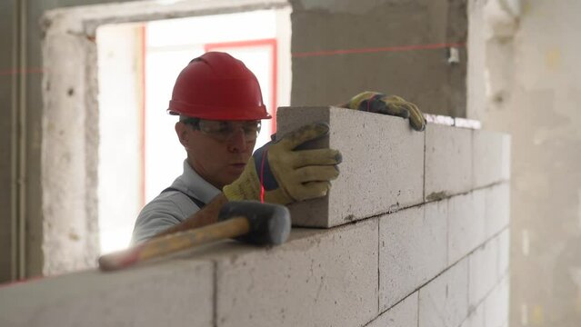 Bricklayer or mason lays bricks to construct wall of autoclaved aerated concrete blocks. Brickwork worker contractor constructs blockwork with foam concrete doing precise masonry with a laser level.
