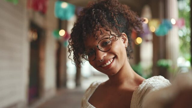 Closeup portrait of a young woman in glasses smiling posing on smartphone selfie camera. Positive woman using mobile phone outdoors in urban background.
