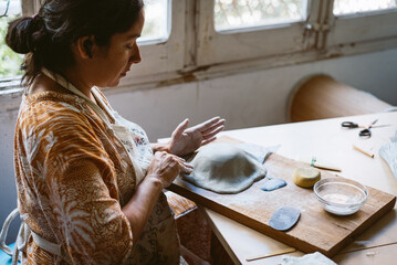Young woman working clay and ceramic at home, making handmade pottery and bowls. Concept of...
