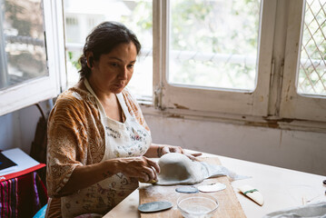 Young woman working clay and ceramic at home, making handmade pottery and bowls. Concept of...