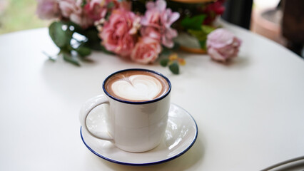 Latte art hot coffee with tulip milk latte art on top of white ceramic glass set on table in coffee shop Hot chocolate drink with white foam and cacao brown powder on top in short cup.