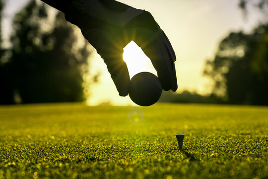 Golfer wearing glove placing golf ball on a tee at golf course