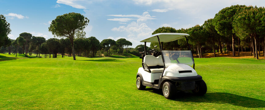 Golf cart on a golf course with green grass field with blue sky and trees