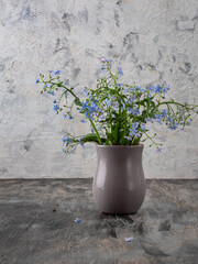 A small bouquet of blue forget-me-nots in a gray ceramic glass