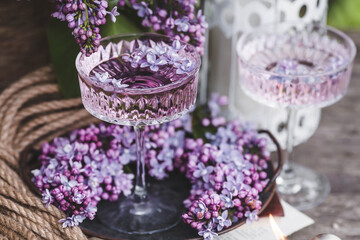 A candle and fancy glasses for dessert and champagne with a lilac drink and lilac flowers inside. The fashionable shade of 2022 is very relevant. The concept of a party and a holiday. Still-life.