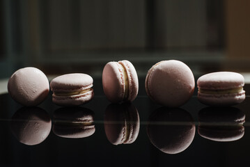 French pink macarons on a black background. Raspberry macaron with white ganache filling. French meringue cookies macaron. Dark background.  film noise