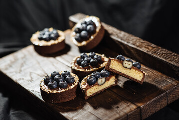 Chocolate tartlets decorated with blueberries on a dark wooden background. Beautiful portion cakes for the holiday table. Dessert with fresh blueberries.