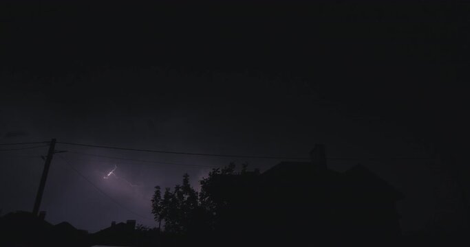 Flashes of lightning over the night street illuminate the house. Strong storm with thunder