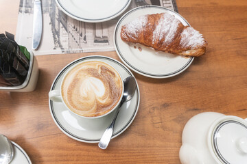 Cup of cappuccino coffee and croissant close-up top view.