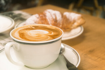 Cup of cappuccino coffee and croissant close-up top view.
