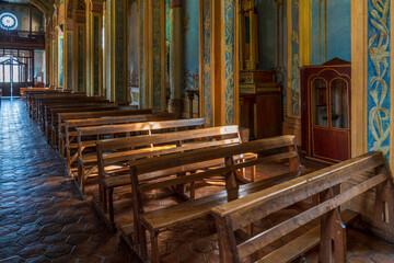 Fototapeta na wymiar There are hundreds of medieval churches in Cuenca, Ecuador. In a simple chapel, the afternoon sun shines on the pews of the church.