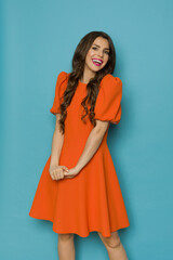 Vibrant young woman is posing in orange cocktail mini dress with puffed short sleeves.