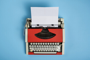 Top view of red vintage typewriter with white blank paper sheet