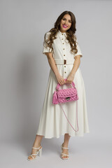 Beautiful woman in white maxi dress holding pink braided purse.