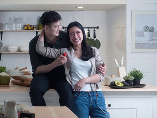 Sweet Asian young adult couple having a wonderful time together in the kitchen at home. Just married couple smiling with happiness.