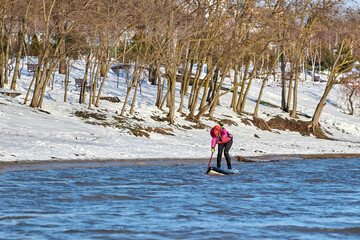Girl paddler is paddling a stand up paddleboard on winter Danube river near shore. Winter scenery
